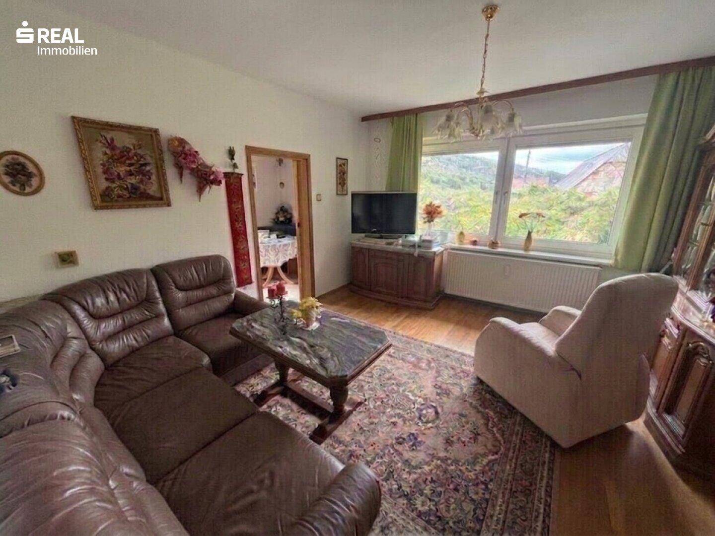 Wohnzimmer mit Ledersofa, Teppich und großem Fenster mit Blick ins Grüne.