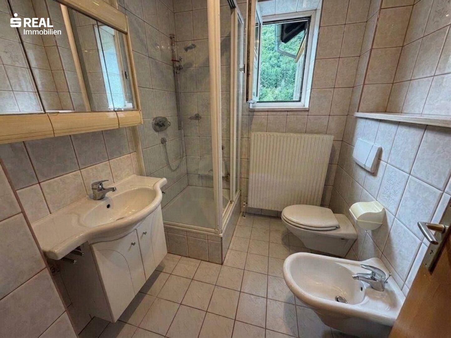 Gefliestes Badezimmer mit Dusche, Waschbecken, WC und Bidet, sowie einem Fenster.