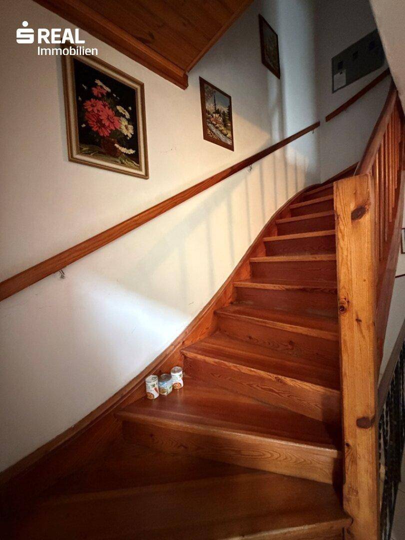 Holztreppe mit Geländer, die in die obere Etage führt, mit Bildern an der Wand.