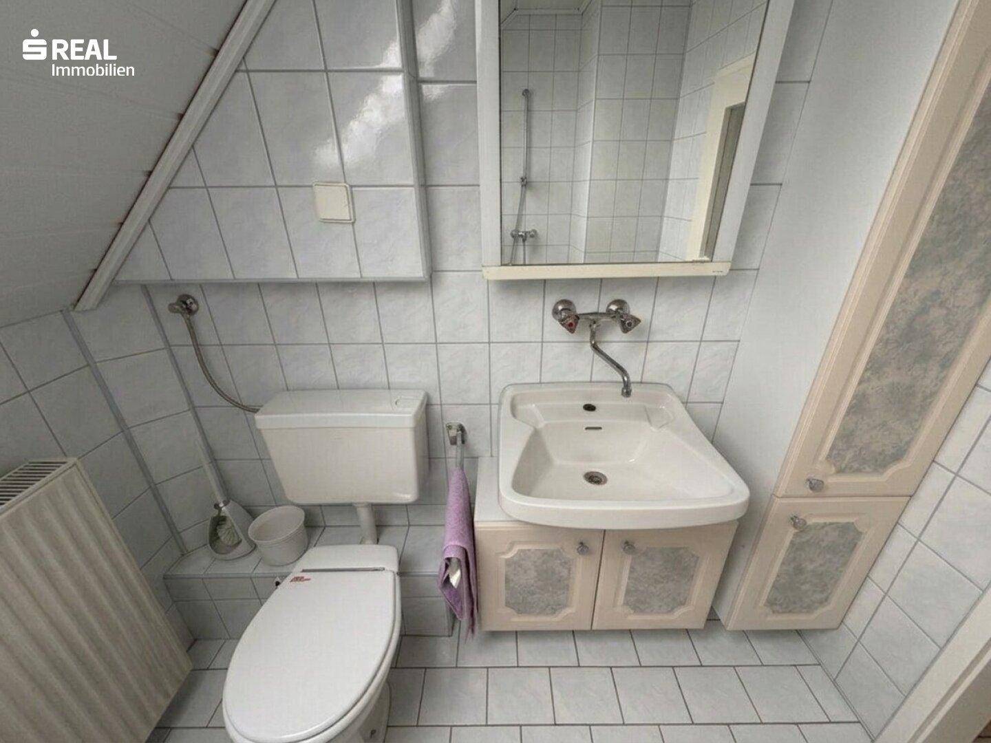 Kleines Badezimmer mit Waschbecken, WC, Spiegel und weißen Fliesen.