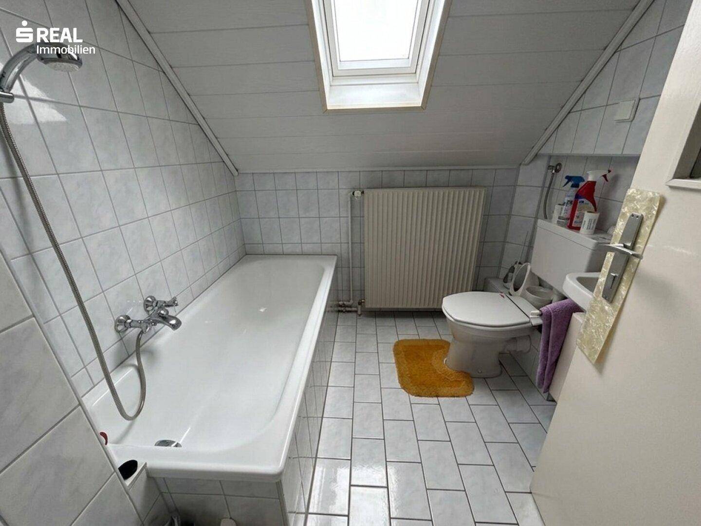 Gefliestes Badezimmer im Dachgeschoss mit Badewanne, WC und Dachfenster.