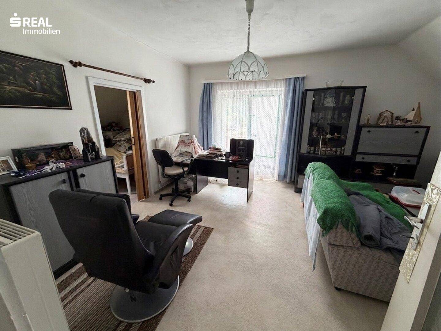 Arbeitszimmer mit Schreibtisch, Sessel und Fenster, das viel Tageslicht hereinlässt.