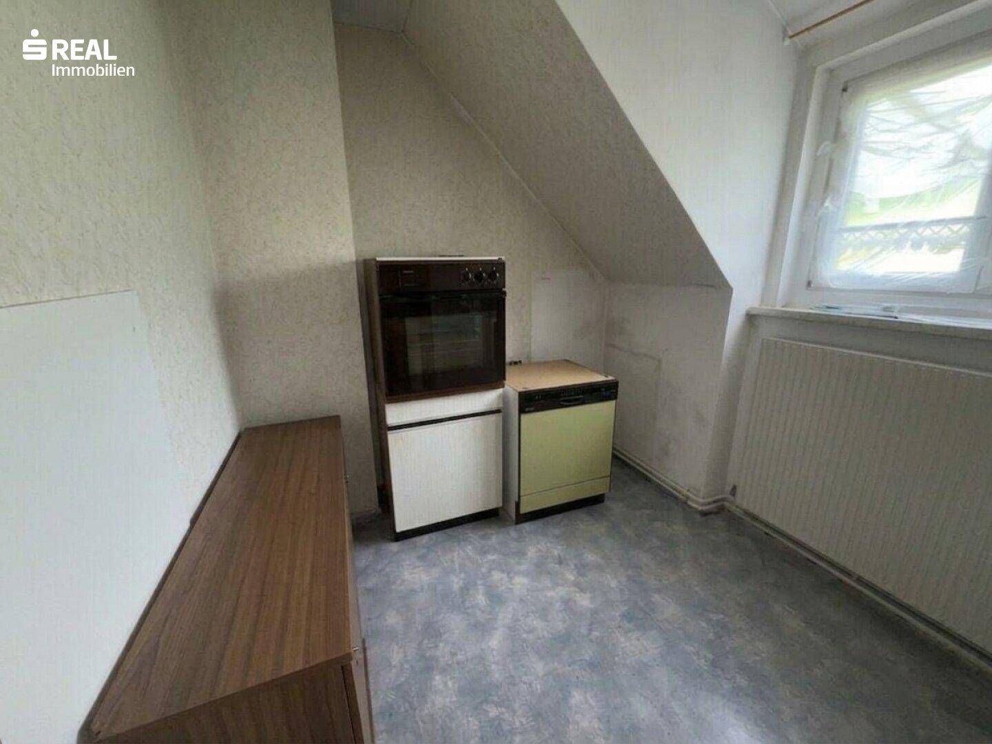 Dachgeschossküche mit schrägen Wänden, Einbaugeräten und kleinem Fenster.