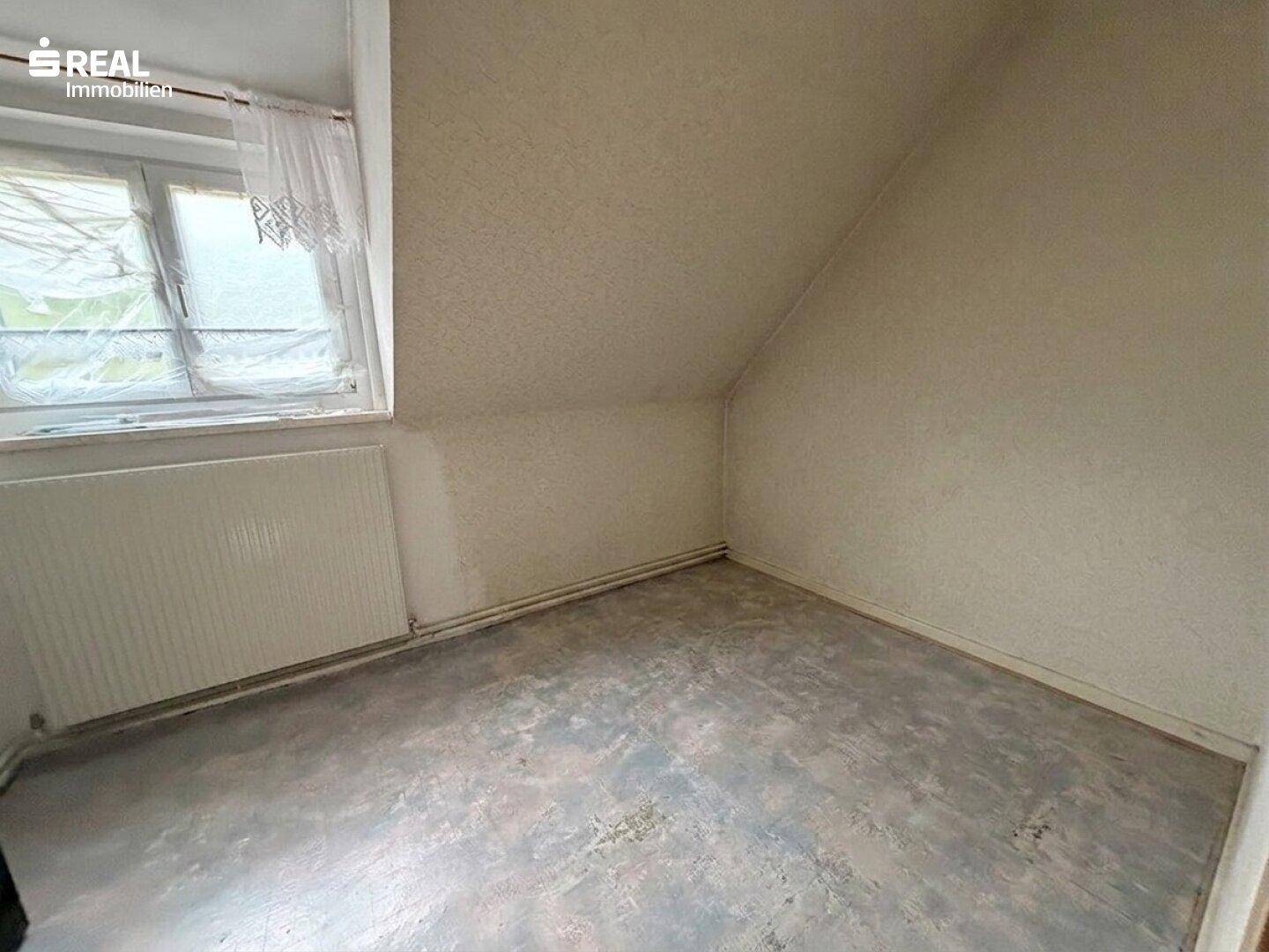 Dachgeschossraum mit schrägen Wänden, kleinem Fenster und Heizkörper.