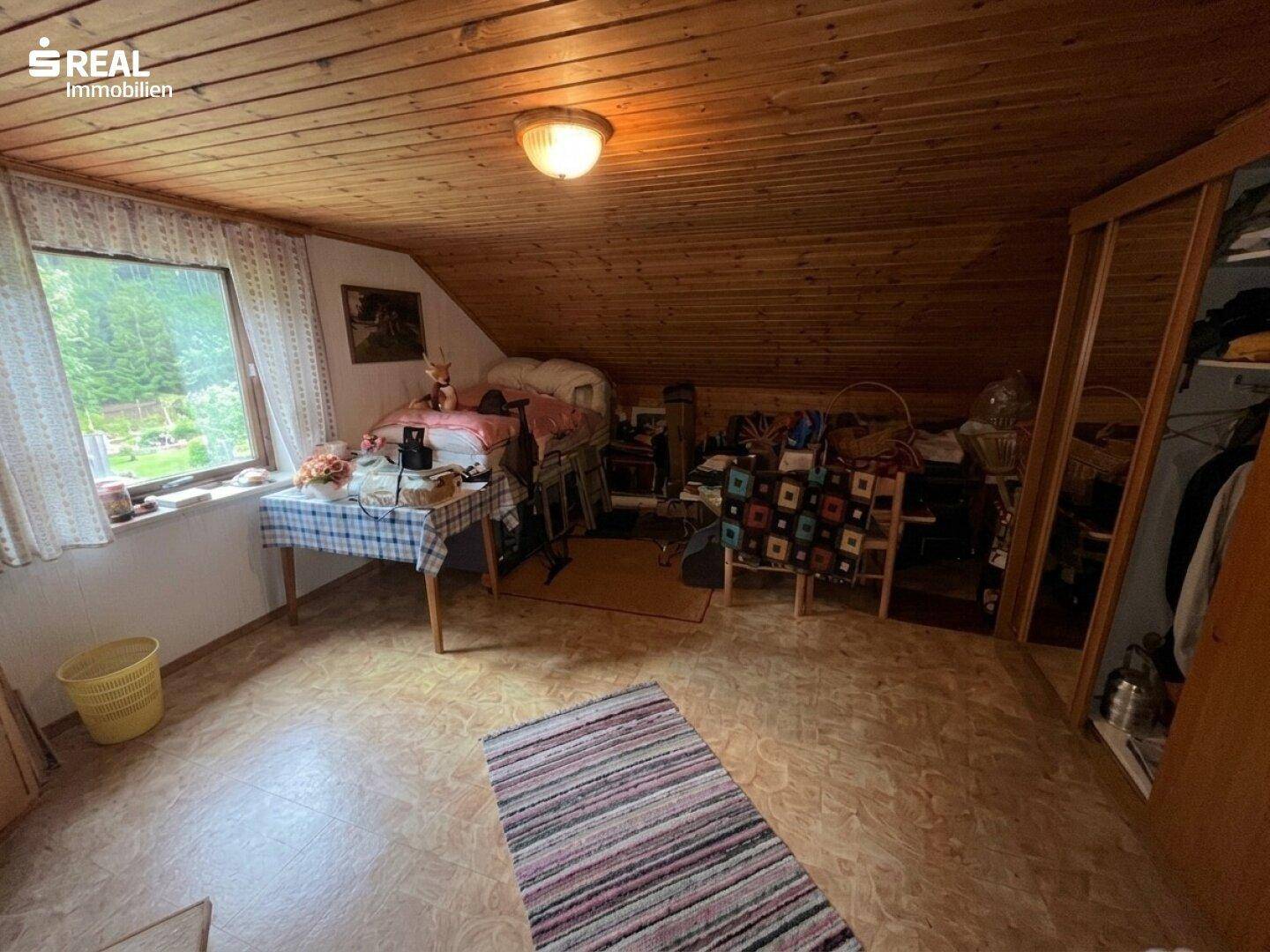 Gemütlicher Dachgeschossraum mit Holzverkleidung, Fenster und Teppichboden.