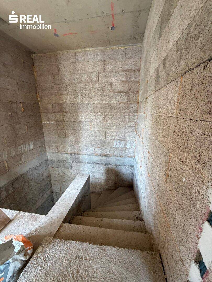 Rohbautreppe aus Beton in einem unfertigen Innenbereich mit unverputzten Wänden.
