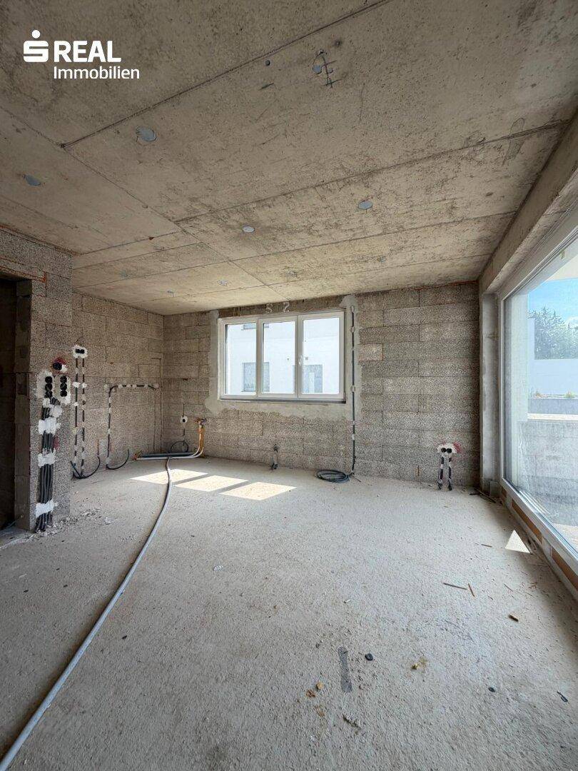 Rohbauzimmer mit unverputzten Wänden, Fenster und vorbereiteten Elektroinstallationen.