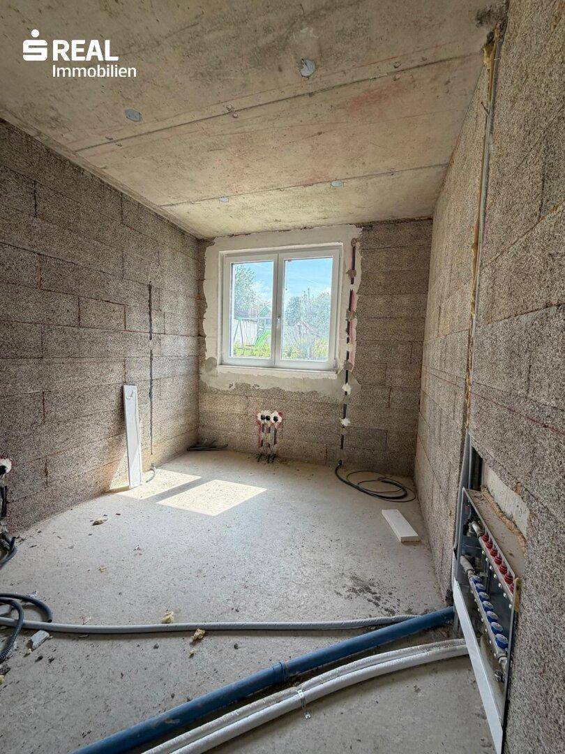 Rohbauzimmer mit vorbereiteten Sanitärinstallationen und Fenster, möglicherweise ein Badezimmer.