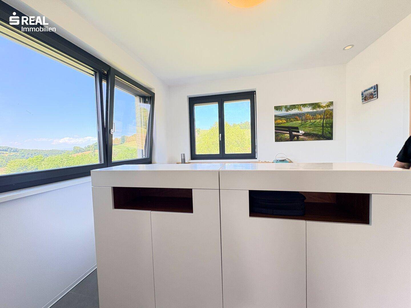 Helle Küchenzeile mit weißer Arbeitsplatte und großen Fenstern mit weitem Ausblick.