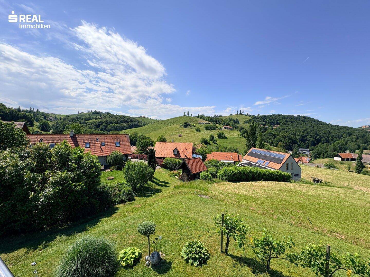 Weitläufiger Blick über die grüne Hügellandschaft mit verstreuten Häusern und Weinreben.