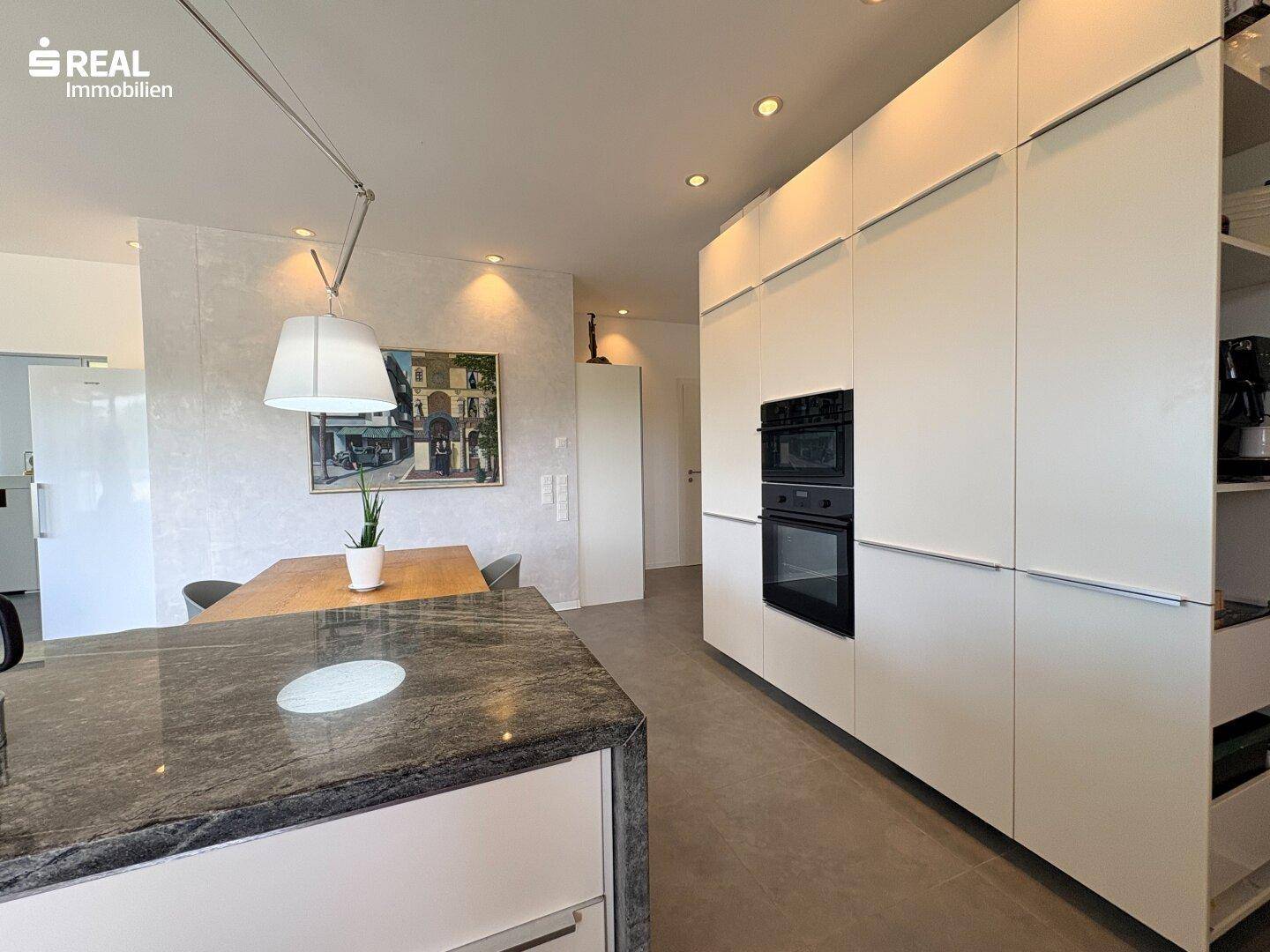 Elegante weiße Einbauküche mit dunkler Arbeitsplatte und integriertem Backofen.