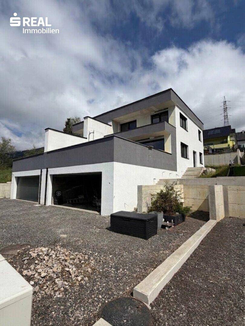 Seitenansicht eines modernen Hauses mit integrierter Garage und Treppenaufgang im Freien.