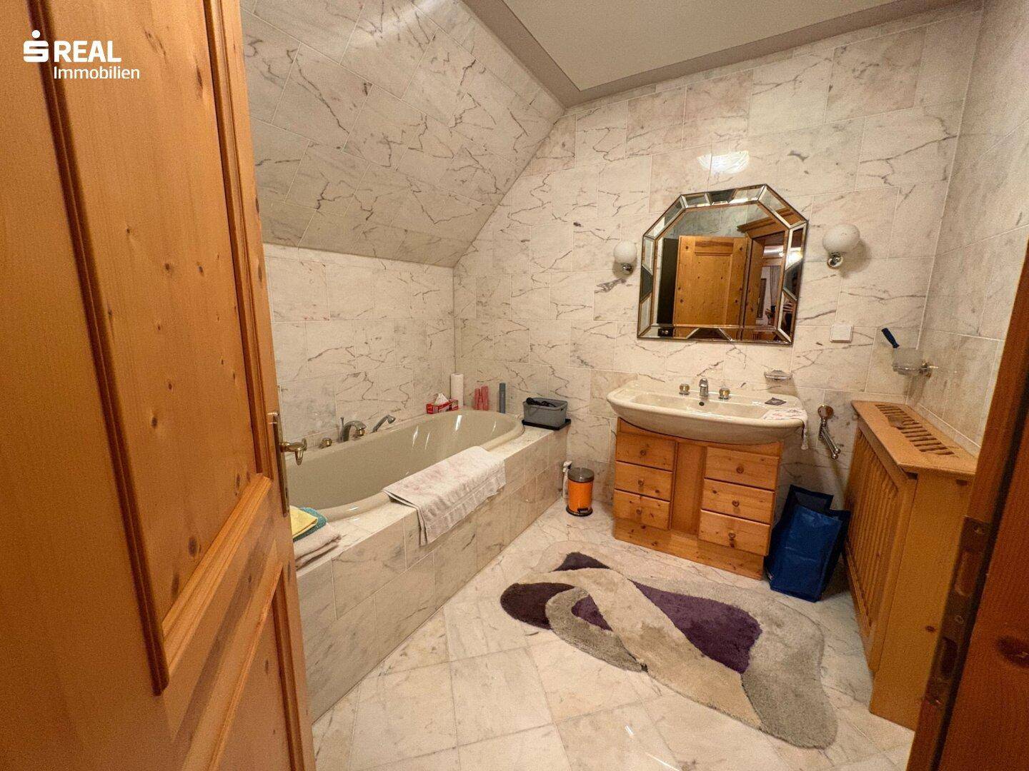 Badezimmer mit Marmorfliesen, Badewanne und Holzwaschtisch unter Dachschräge.