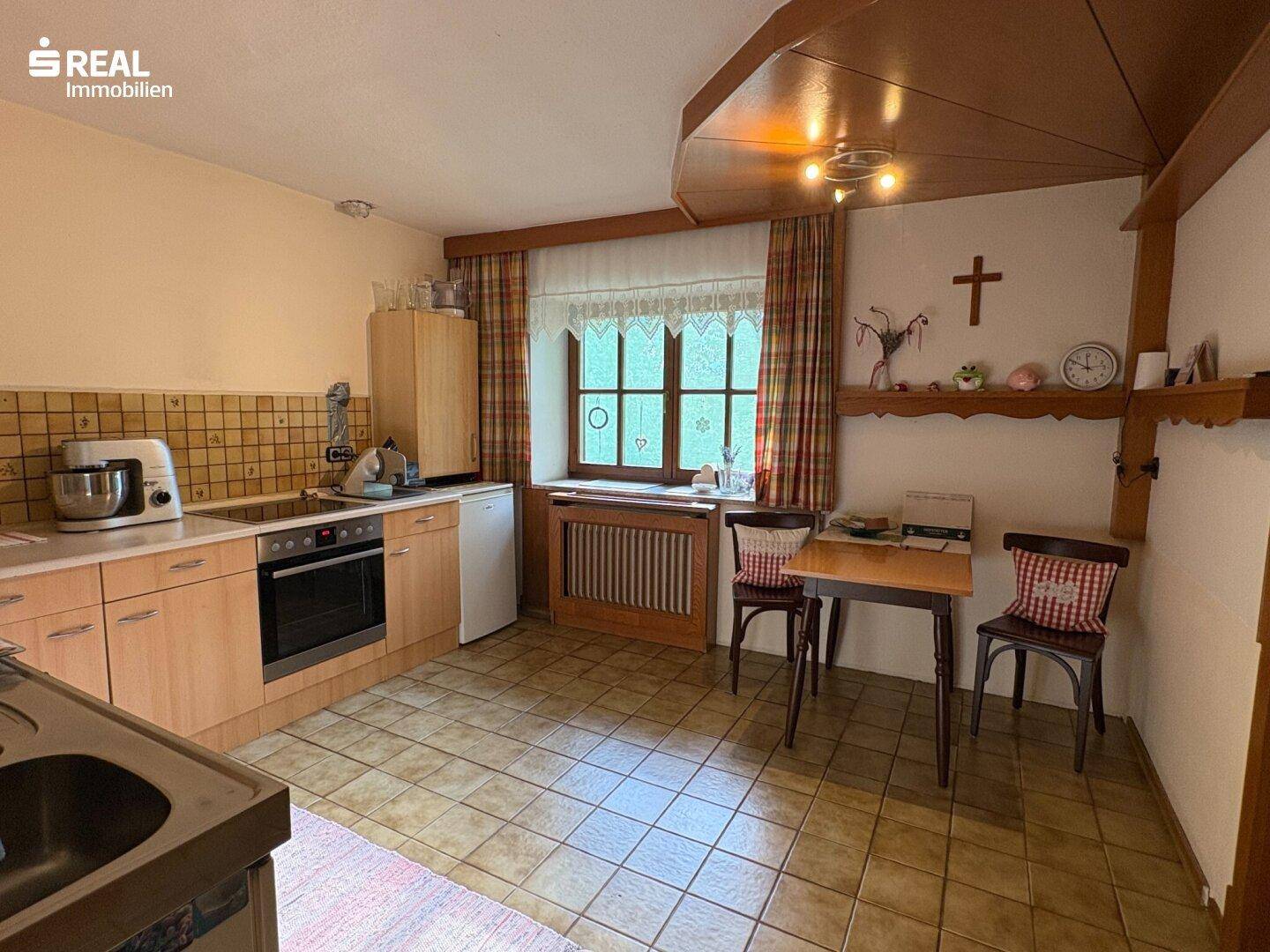 Traditionelle Küche mit Holzschränken, Fliesenboden und Essbereich am Fenster.