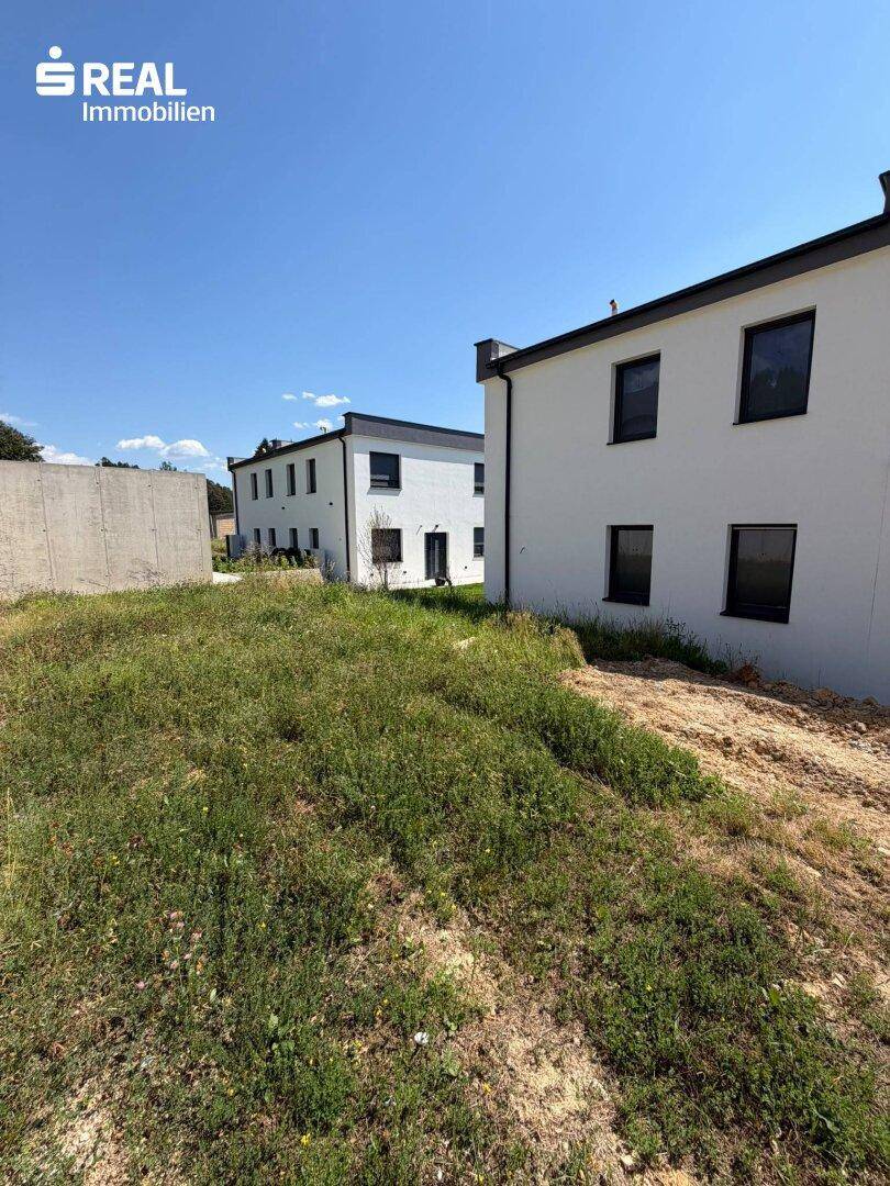 Zwei moderne Neubauten mit weißer Fassade und dunklen Fenstern in einer ländlichen Umgebung.