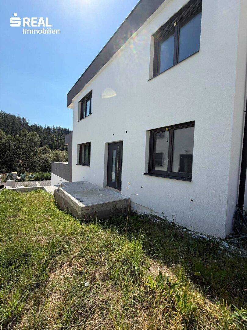 Seitenansicht eines modernen Hauses mit weißer Fassade und Zugang zum Gartenbereich.