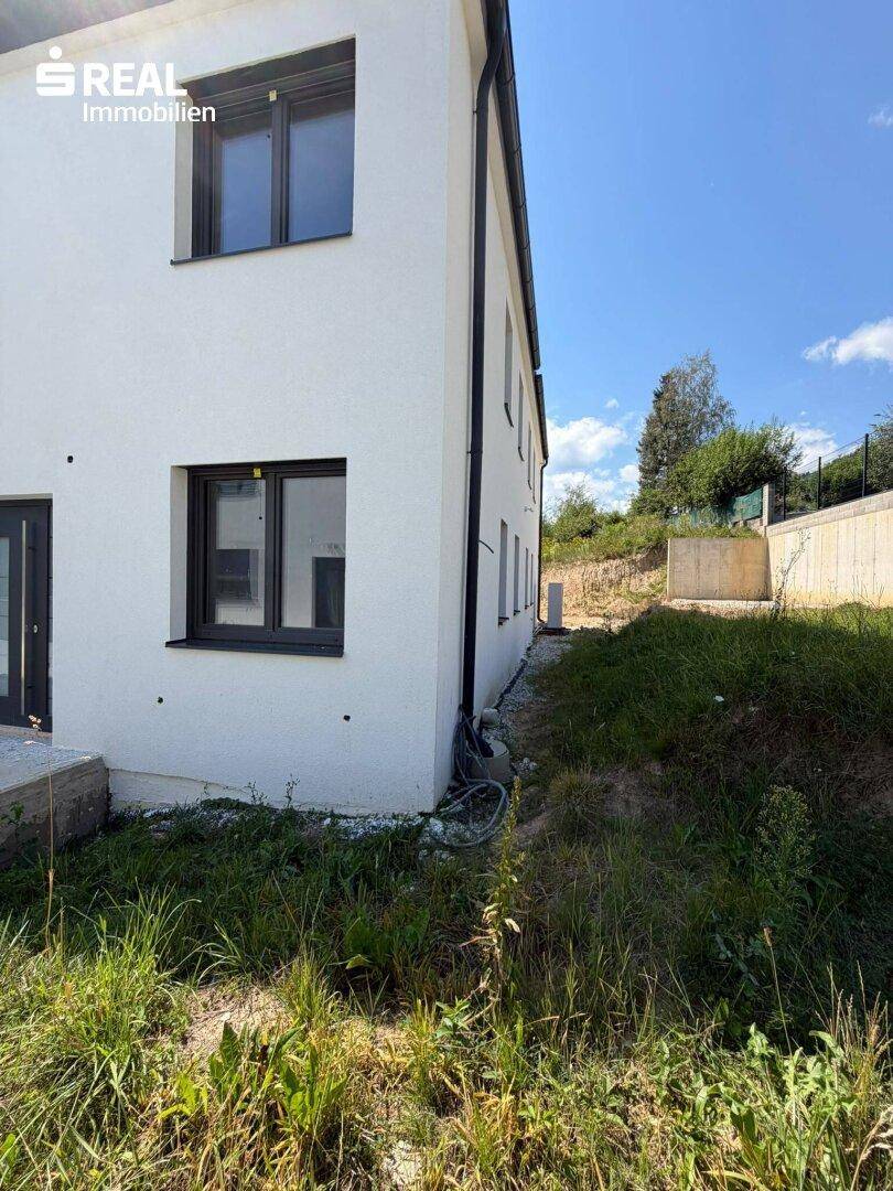 Seitenansicht eines modernen Hauses mit weißer Fassade und Blick auf die umliegende Natur.