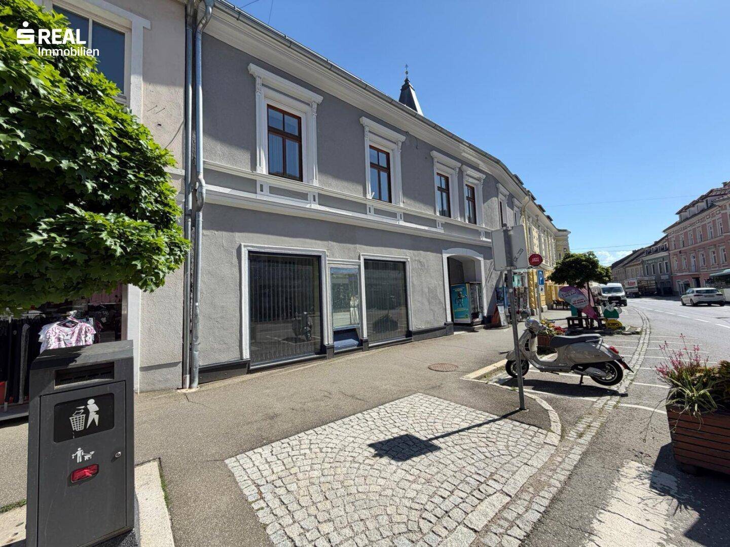 Nahaufnahme der Fassade eines Geschäftsgebäudes mit Schaufenstern und Kopfsteinpflaster auf dem Gehweg.