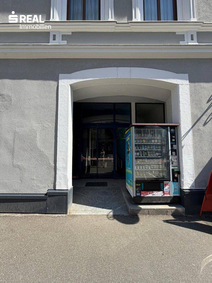 Eingangsbereich eines Gebäudes mit einem Verkaufsautomaten und einer gewölbten Türöffnung.