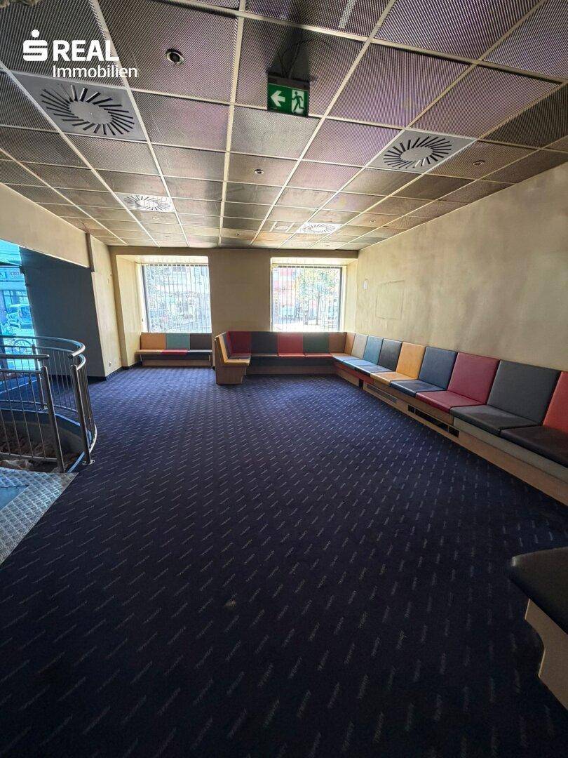 Großer Innenraum mit Teppichboden, langen Sitzbänken und abgehängter Decke mit Beleuchtung.