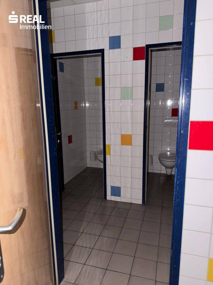 Mehrere Toilettenkabinen mit bunten Fliesen an den Wänden und auf dem Boden.