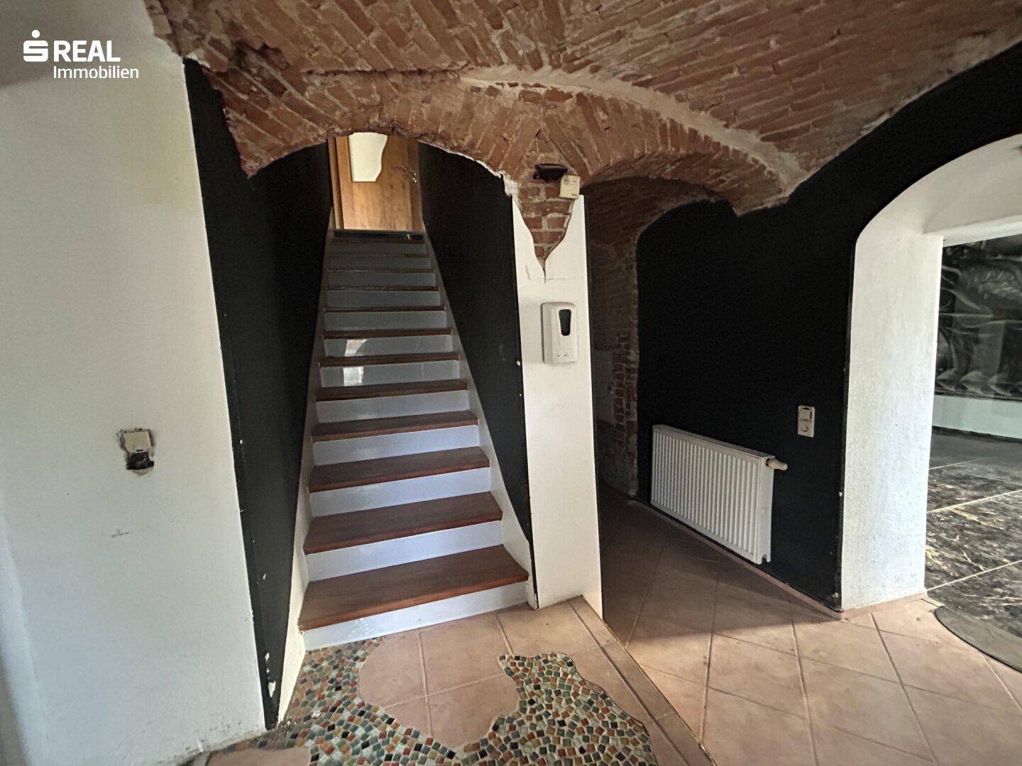 Eingangsbereich mit Treppe, Ziegelgewölbe und gefliestem Boden, der zu weiteren Räumen führt.