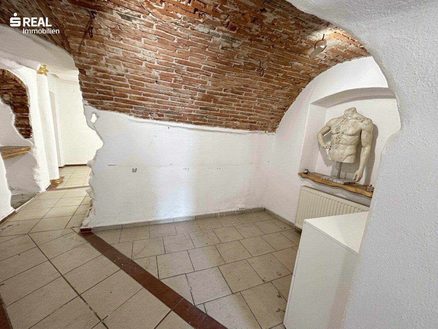 Raum mit freigelegten Ziegelwänden, Fliesenboden und einer Nische mit Statue.