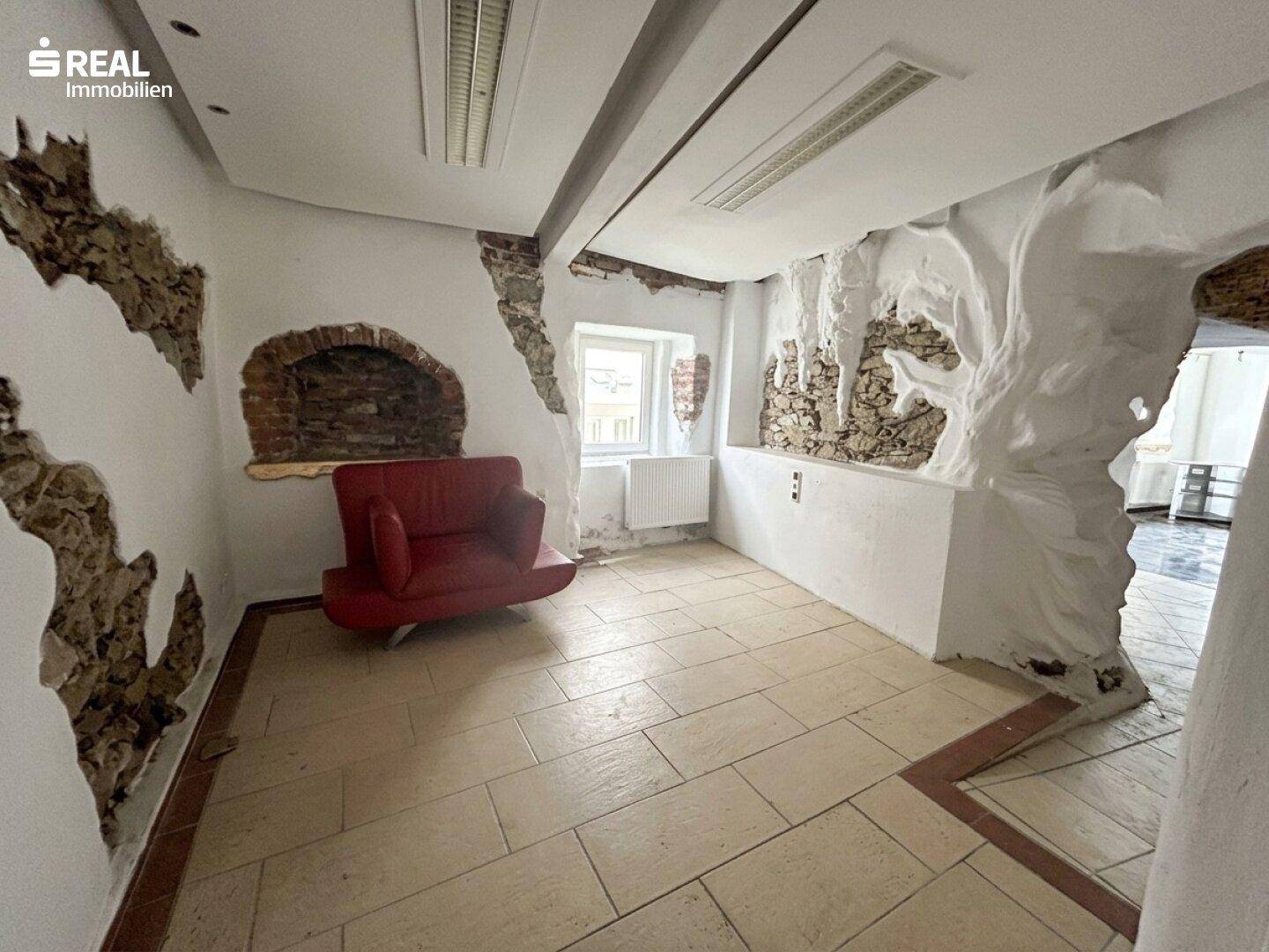 Wohnraum mit Fliesenboden, freigelegten Steinwänden und einem roten Sessel.
