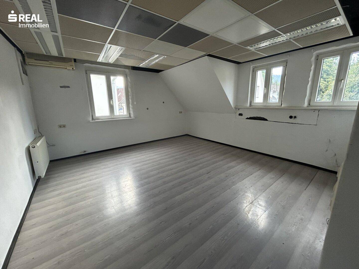 Geräumiges Zimmer mit abgehängter Decke und mehreren Fenstern, geeignet als Büro oder Arbeitsbereich.