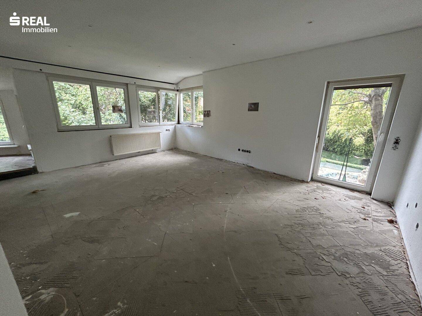 Großer, heller Raum mit vielen Fenstern und unfertigem Boden, ideal für offenes Wohnen.