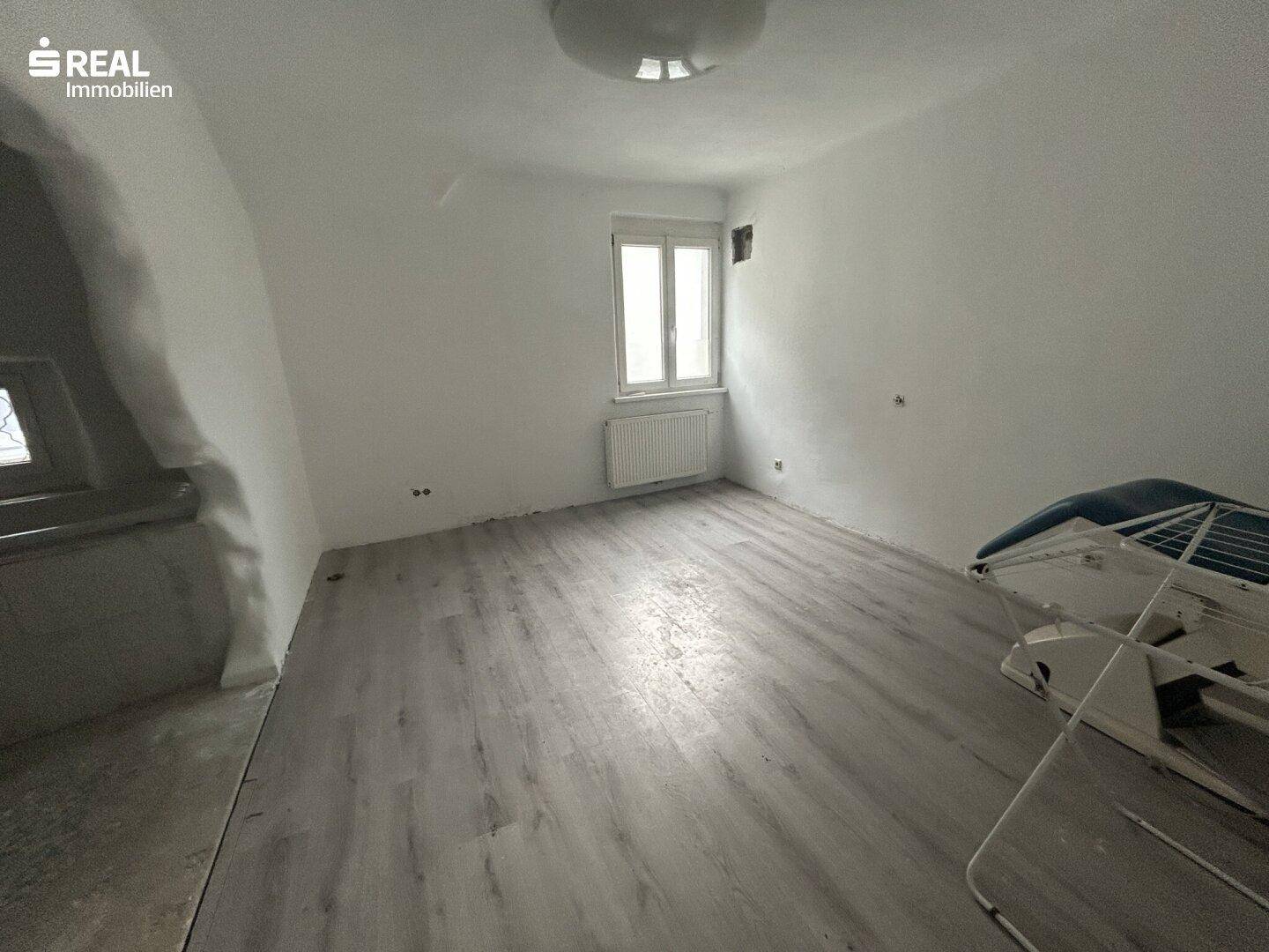 Helles Schlafzimmer mit Laminatboden und einem Fenster, bereit zur individuellen Einrichtung.