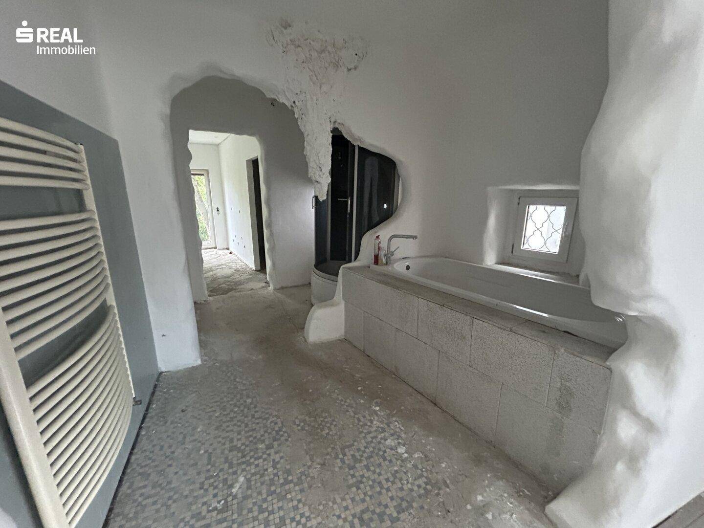 Badezimmer mit Badewanne, Heizkörper und unkonventionellen Wandstrukturen, noch im Umbau.