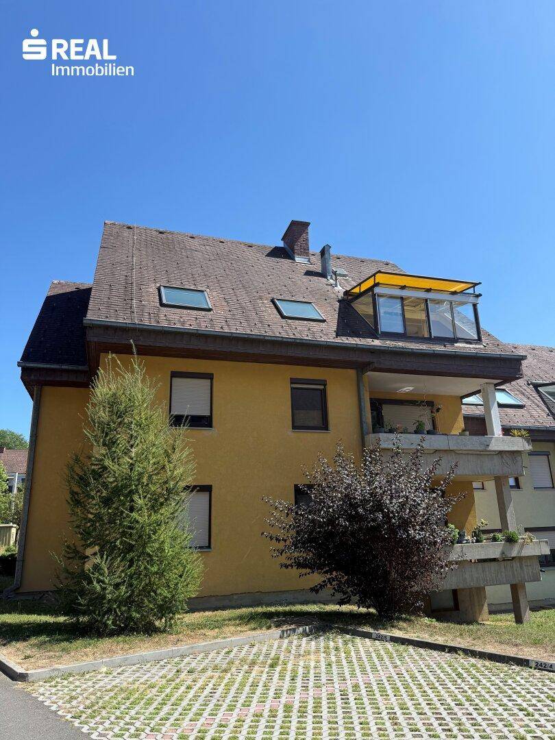 Gelbe Fassade eines Mehrfamilienhauses mit Balkonen und Dachfenstern unter blauem Himmel.
