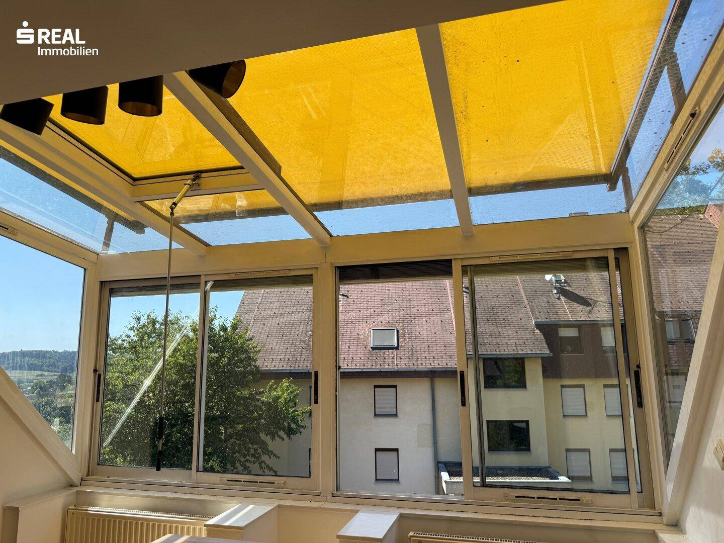 Heller Wintergarten mit gelbem Sonnenschutz und weitem Blick über die Dächer der Nachbarschaft.