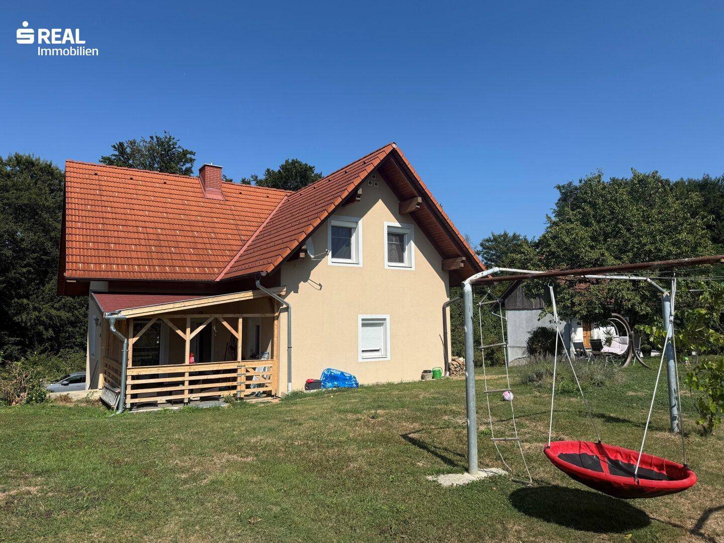 Einfamilienhaus mit großem Garten, Kinderschaukel und überdachtem Holzvorbau in sonniger Lage.
