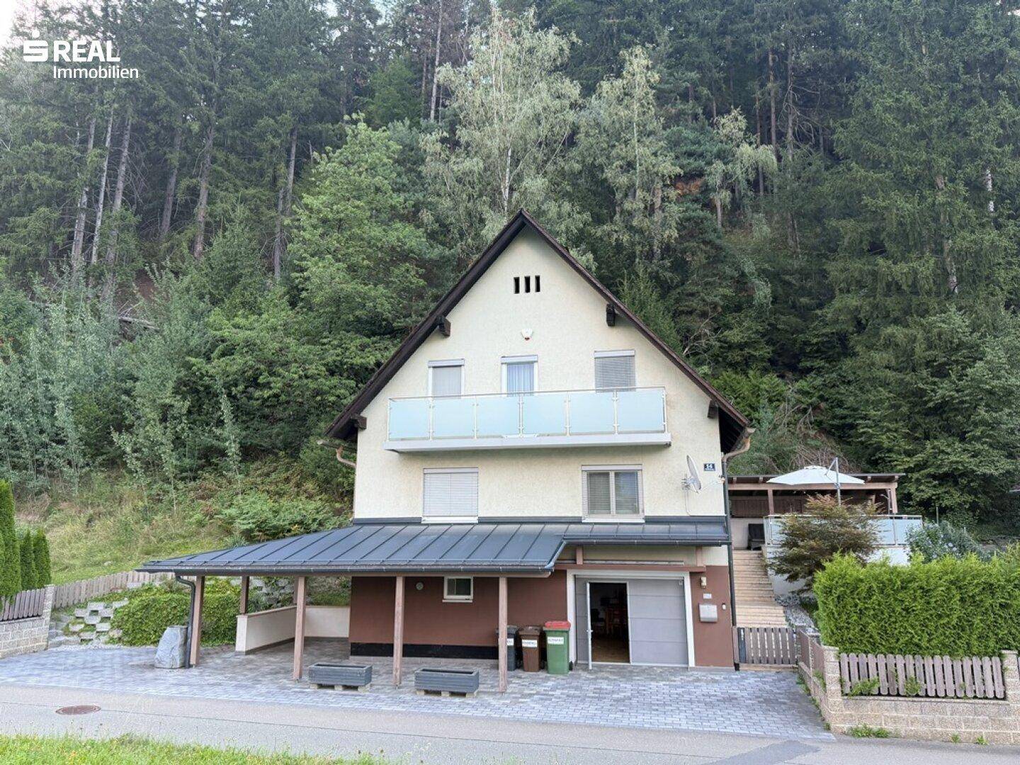 Vorderansicht des Einfamilienhauses mit Carport und Balkon, umgeben von viel Grün.