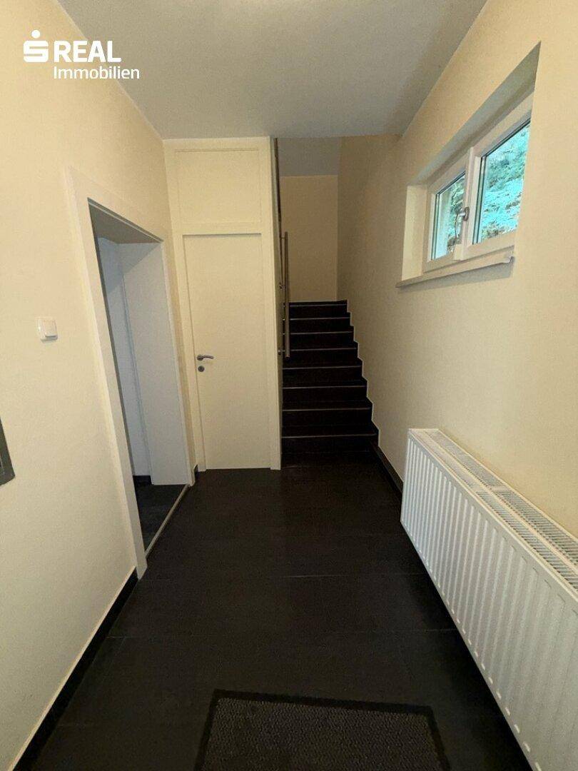 Flur mit dunklem Fliesenboden, Heizkörper und Treppe zum Obergeschoss.