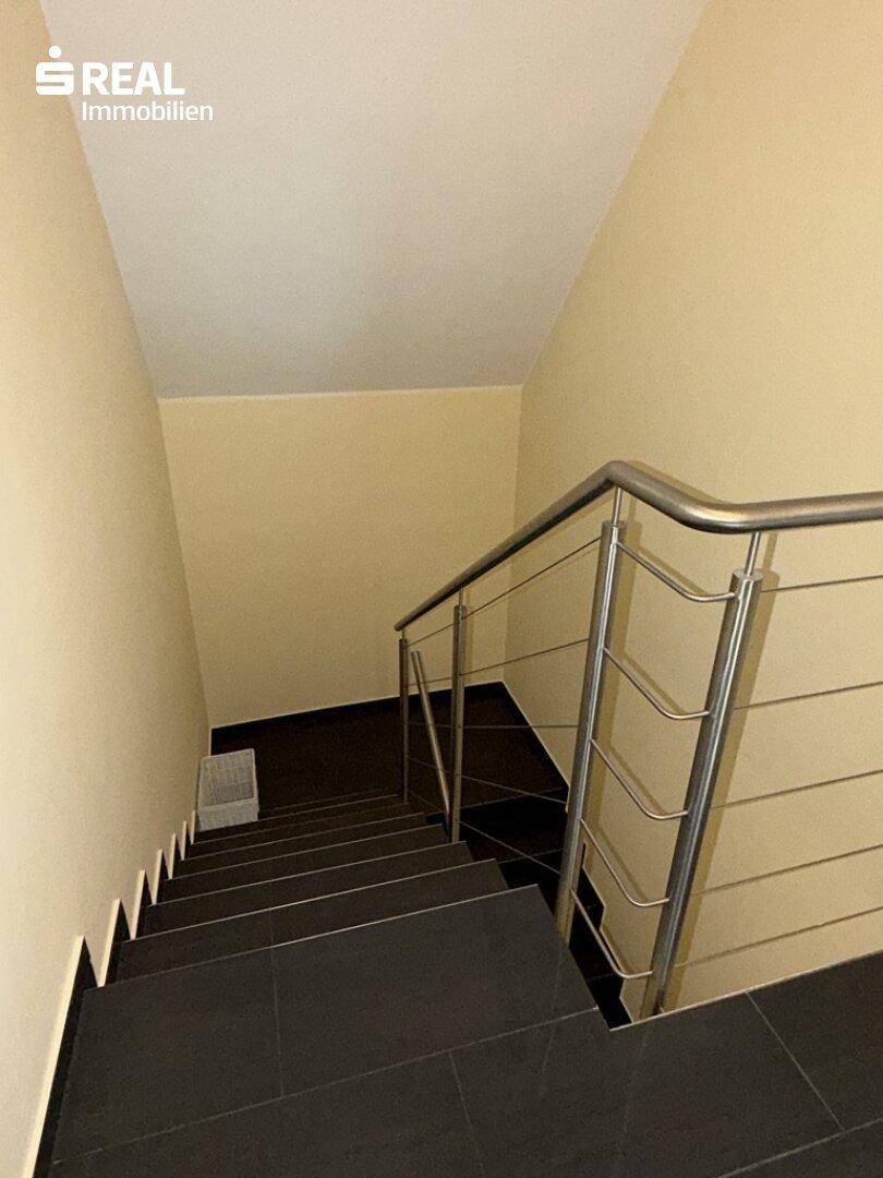 Innentreppe mit dunklen Stufen und modernem Metallgeländer, führt in die oberen Etagen.