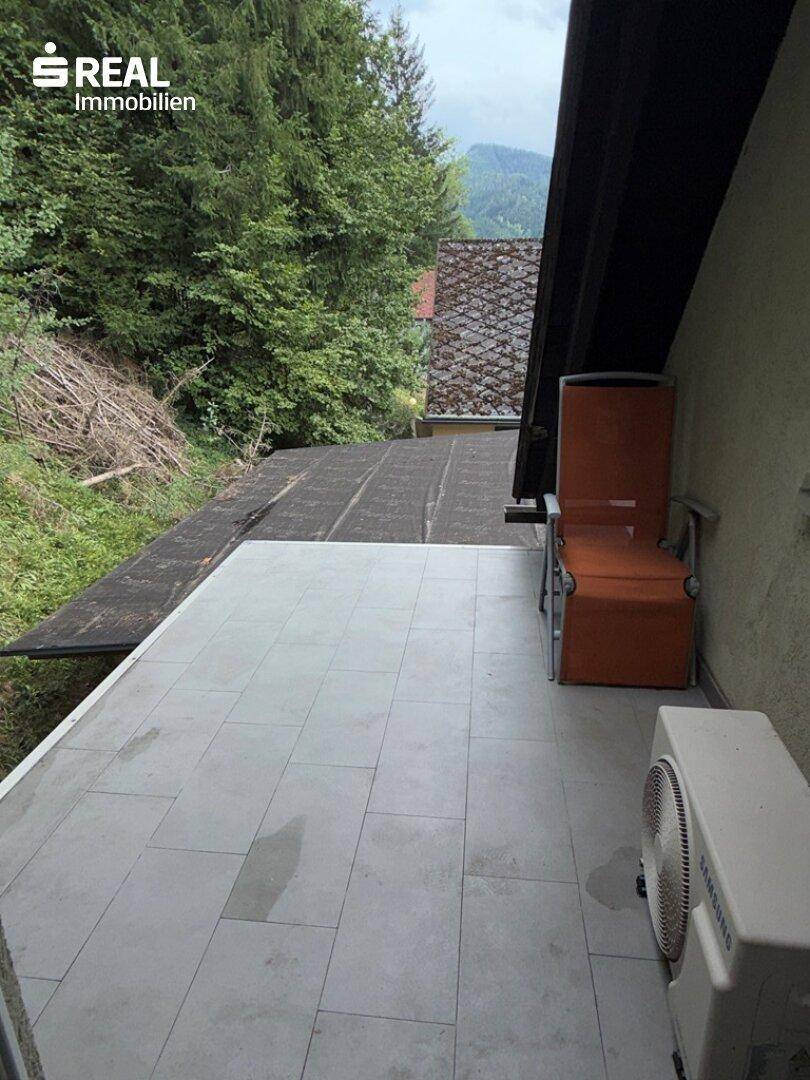 Helle geflieste Terrasse mit einem Stuhl und Blick auf die umliegende grüne Landschaft.
