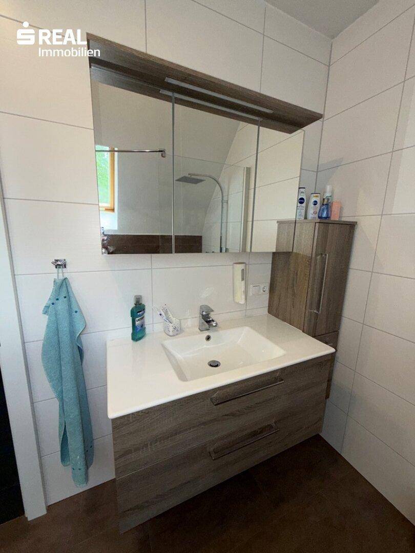 Badezimmer mit modernem Waschtisch, Spiegelschrank und weißen Fliesen, gut beleuchtet.