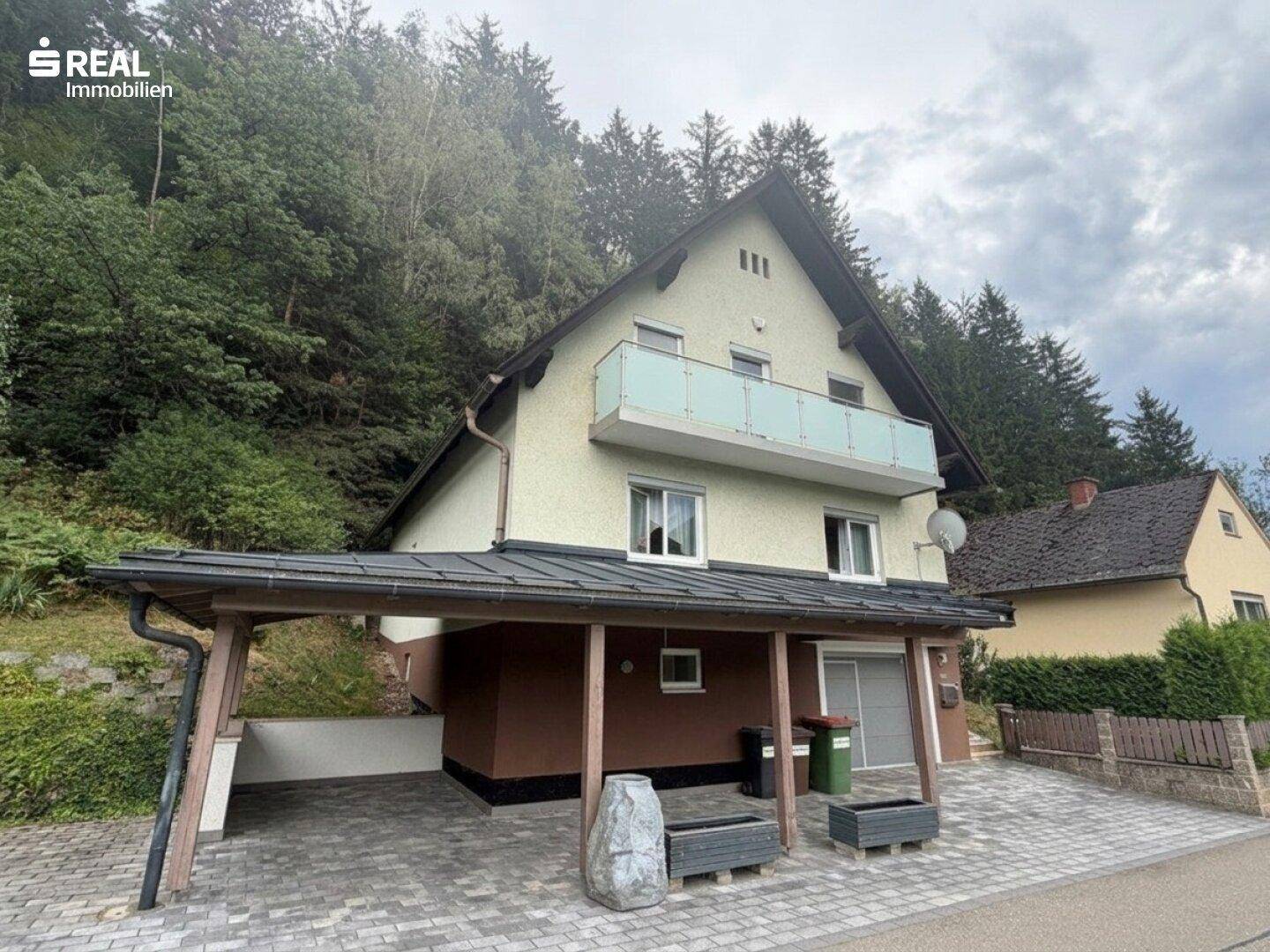 Das Einfamilienhaus mit Carport und Balkon, umgeben von Bäumen und Natur.