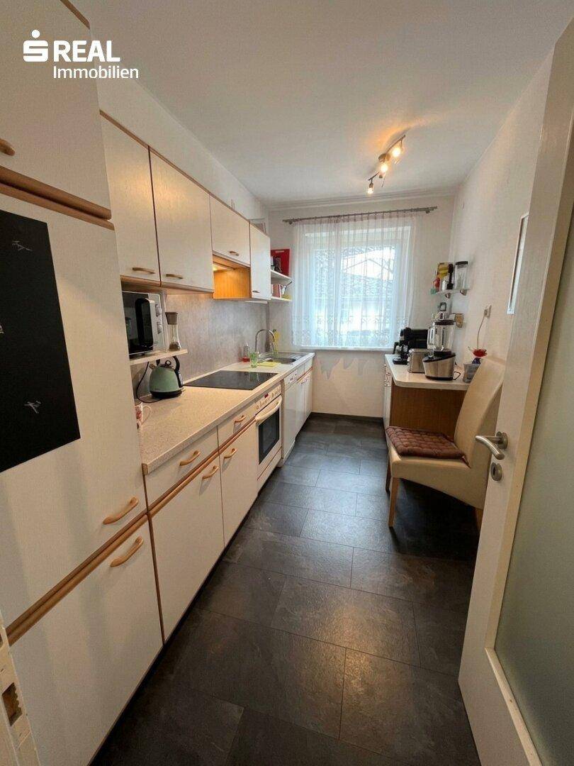 Kleine Küche mit weißen Einbauschränken, dunklem Fliesenboden und Fenster.