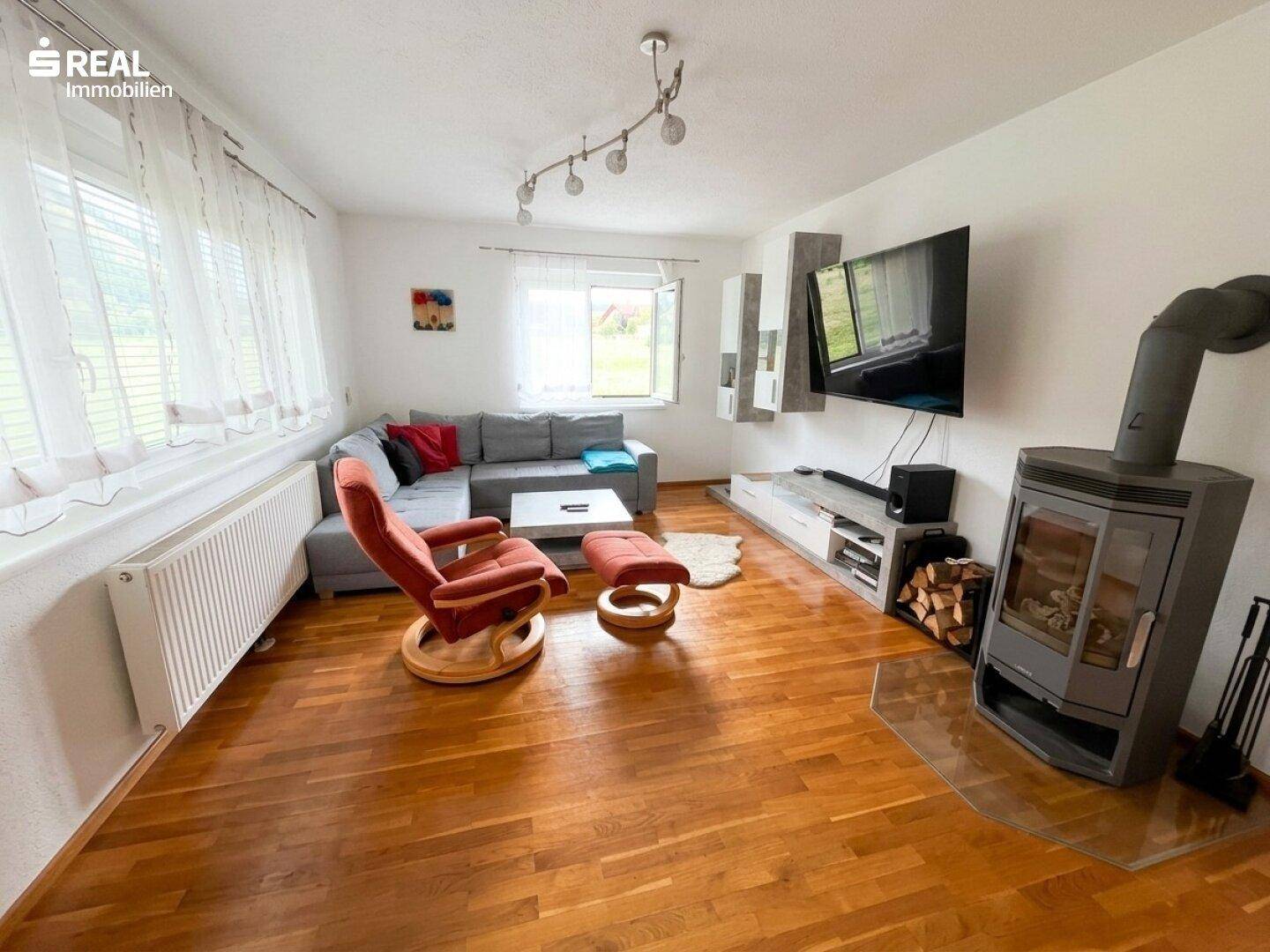 Gemütliches Wohnzimmer mit Holzboden, Ecksofa und einem modernen Holzofen.
