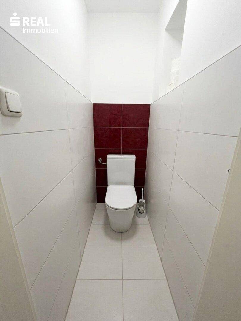 Separates WC mit modernen weißen und roten Fliesen, minimalistisch gestaltet.