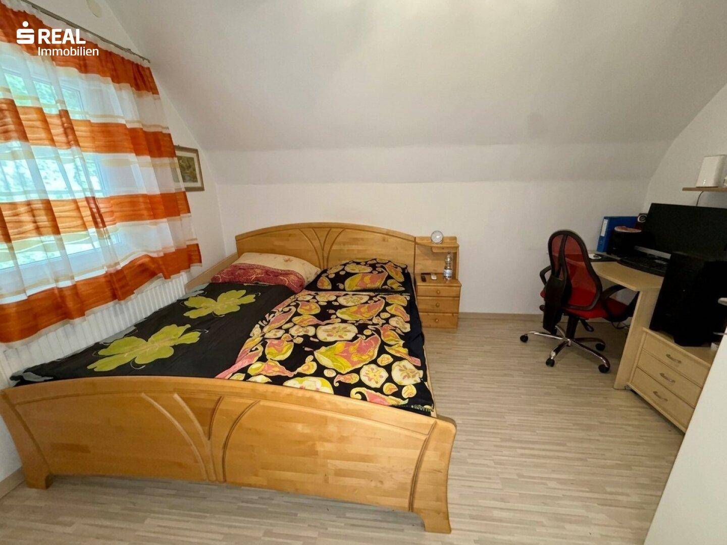 Gemütliches Schlafzimmer mit Holzbett, Schreibtisch und Dachschräge, hell durch Fenster.