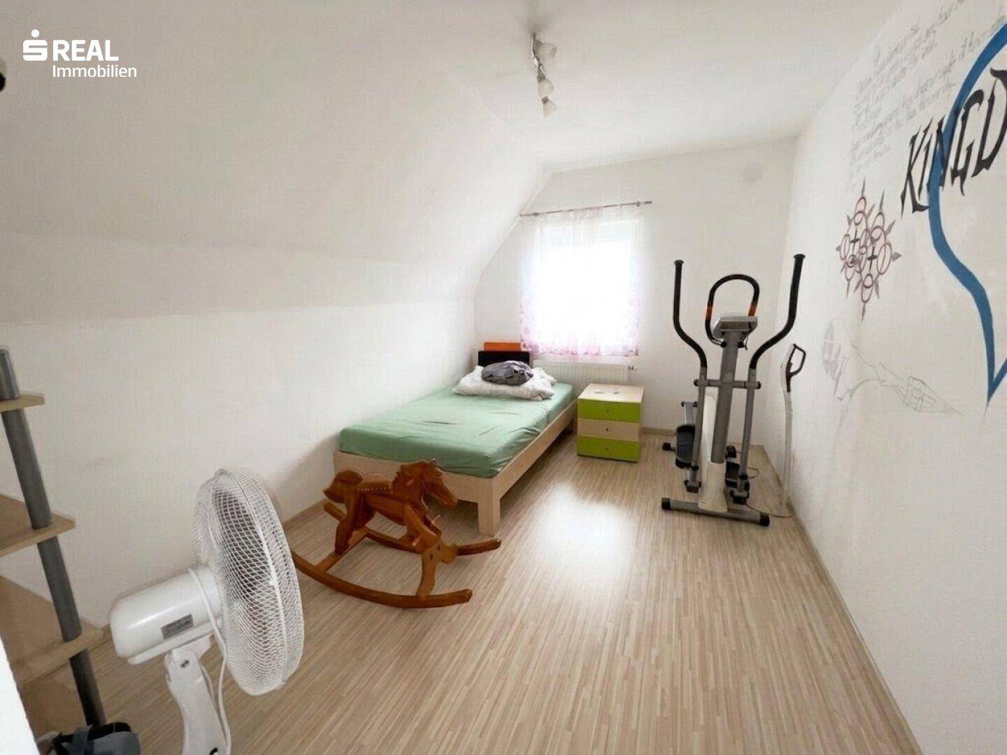 Helles Zimmer mit Einzelbett, Sportgerät und kreativer Wandgestaltung unter der Dachschräge.