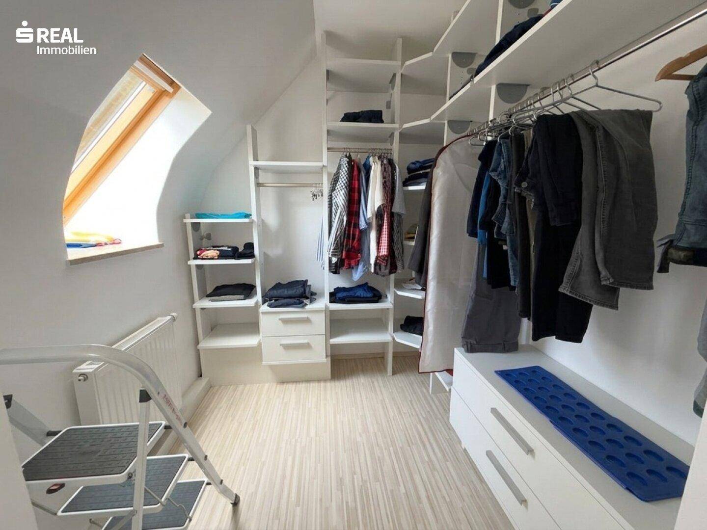 Geräumiger begehbarer Kleiderschrank mit vielen Regalen und Kleiderstangen unter einem Dachfenster.