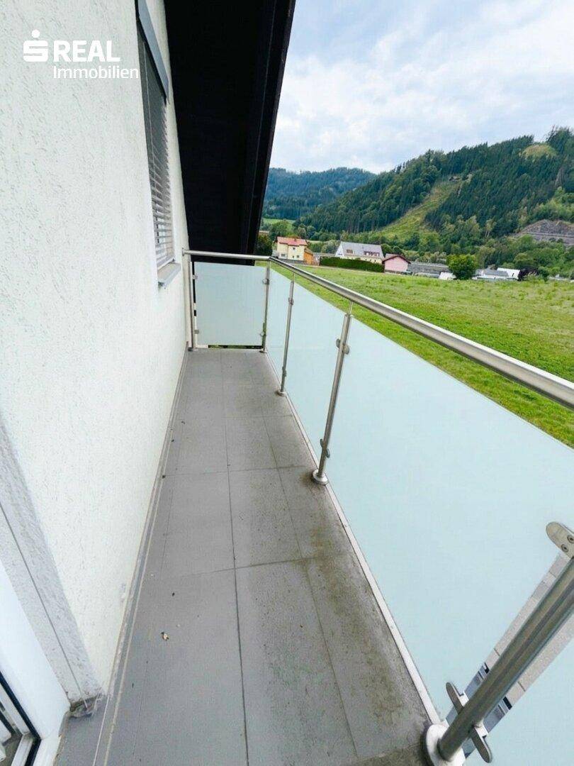 Moderner Balkon mit Glasgeländer und weitem Blick auf grüne Wiesen und Berge.