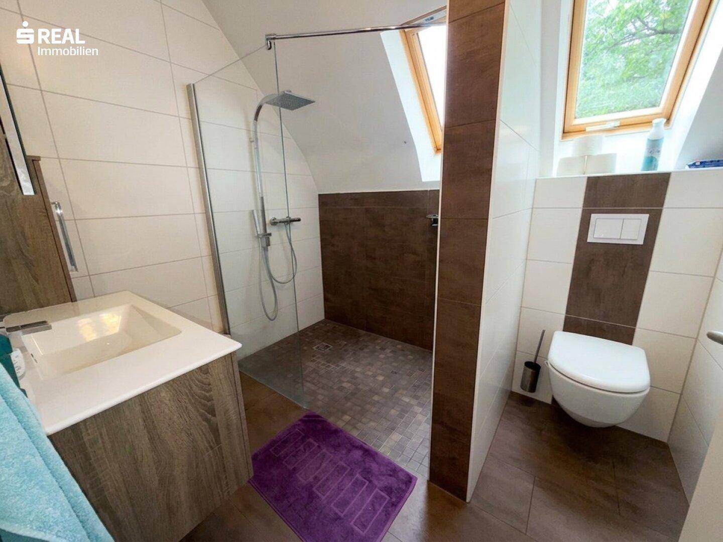 Modernes Badezimmer mit begehbarer Dusche, WC und Dachfenstern für natürliches Licht.