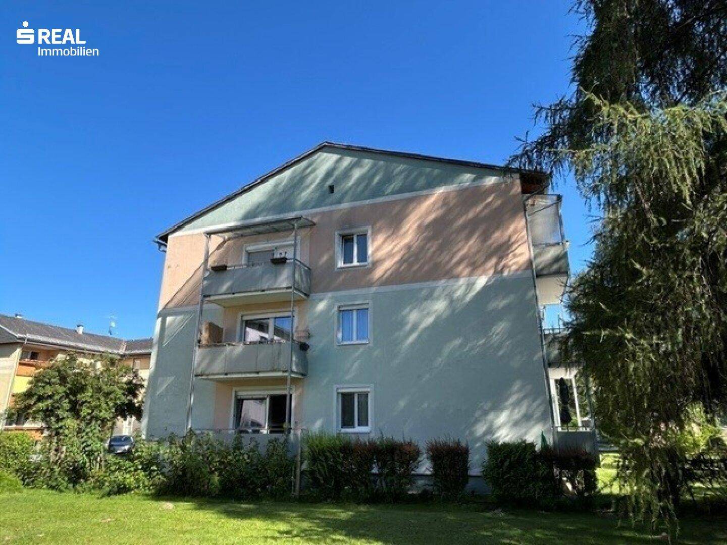 Wohngebäude mit gepflegter Fassade und Balkonen, umgeben von Bäumen und Rasen.